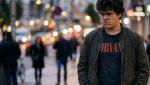 Un adolescente solo paseando por la ciudad, con gesto serio.